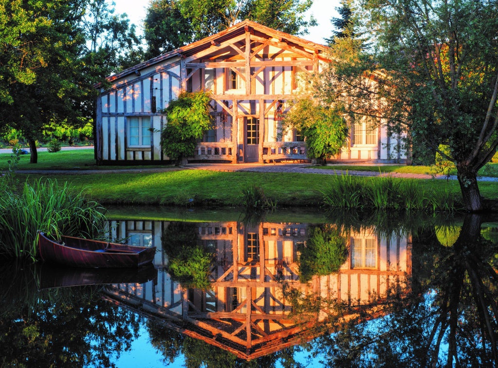 Elegant French vineyard hotel with modern timber-framed buildings surrounded by lush gardens, reflecting in a serene lake at sunset