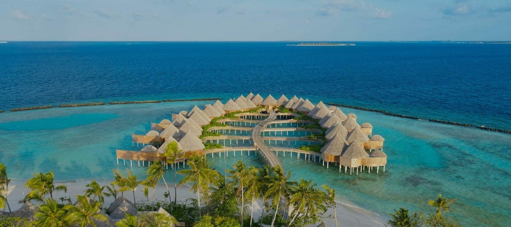 Luxurious overwater villa with curved thatched roof and private infinity pool extending over turquoise Maldivian lagoon at sunset