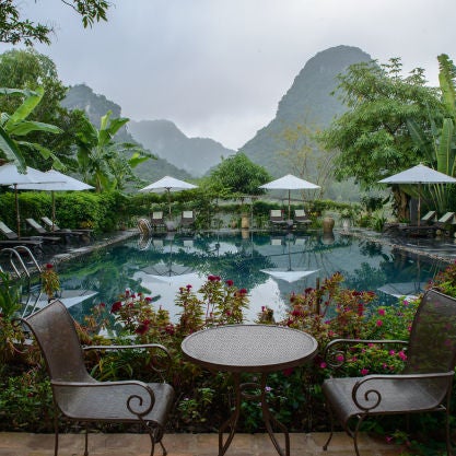 Serene Vietnamese resort villa nestled among limestone peaks, with traditional thatched roof and tranquil reflection pond surrounded by lush gardens