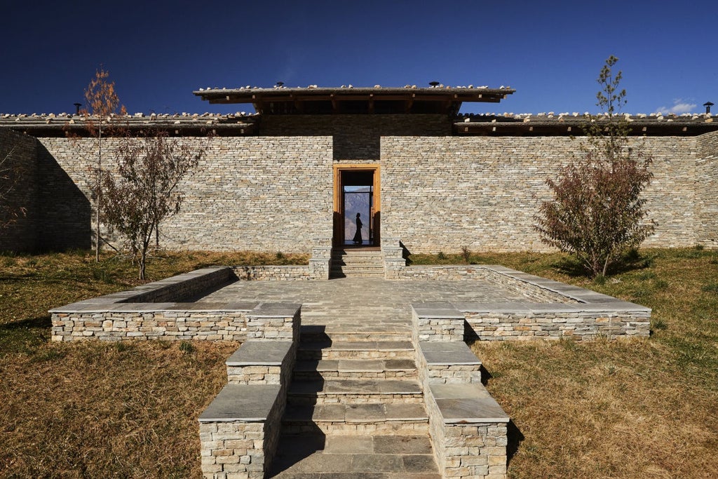 Luxurious mountain lodge with stone facade and wooden beams overlooking snow-capped Himalayan peaks at golden hour in Bhutan