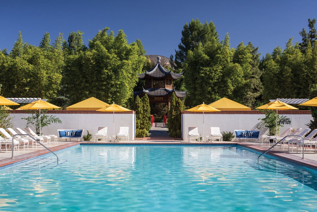 Large modern luxury hotel with Mediterranean-style architecture, palm trees and manicured gardens set against Westlake Village hillside at sunset