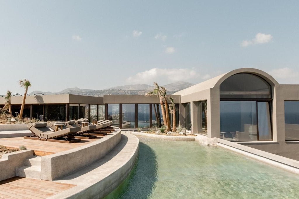 Luxury cliffside suite at Acro Suites overlooking Aegean Sea, featuring infinity pool, natural stone walls and minimalist Greek design