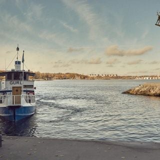 Luxurious waterfront hotel with modern Scandinavian design, white exterior, expansive glass windows overlooking tranquil Swedish coastal landscape at sunset