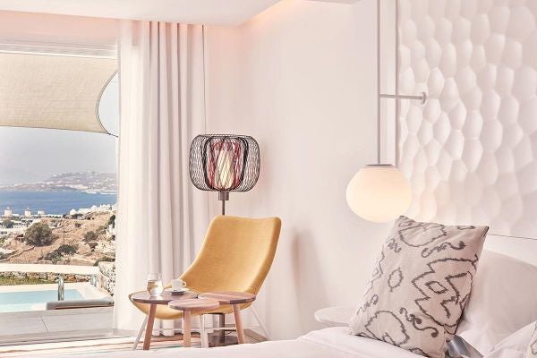 Luxurious white Cycladic hotel overlooking azure Aegean Sea, with infinity pool, minimalist design, and sweeping views of Mykonos coastline at sunset