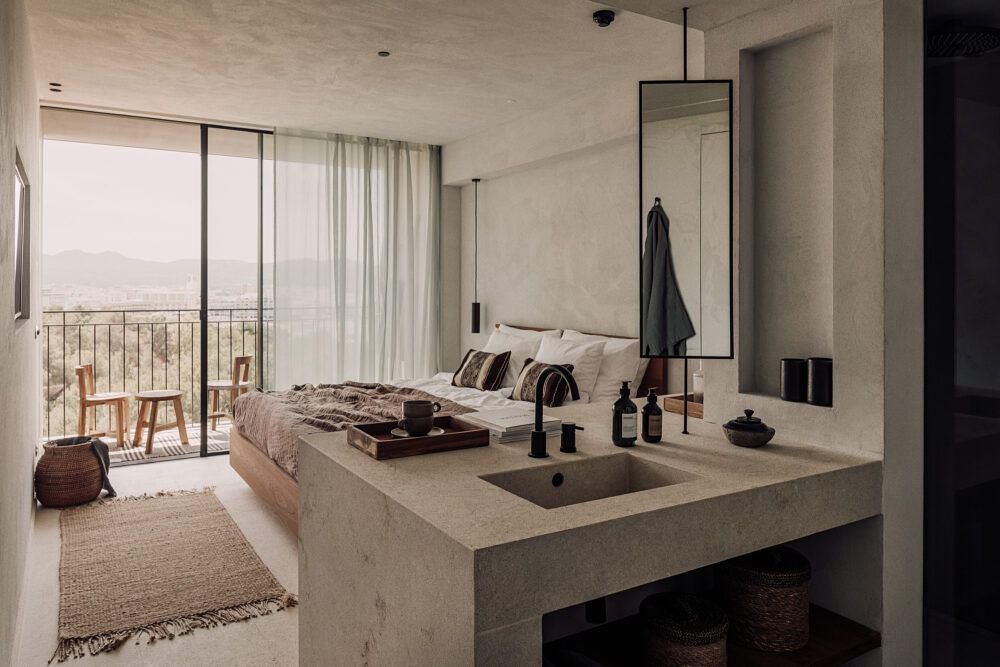 Minimalist white-washed superior room at scenset OKU Ibiza hotel, featuring elegant four-poster bed, natural textures, and soft Mediterranean sunlight streaming through sheer curtains.