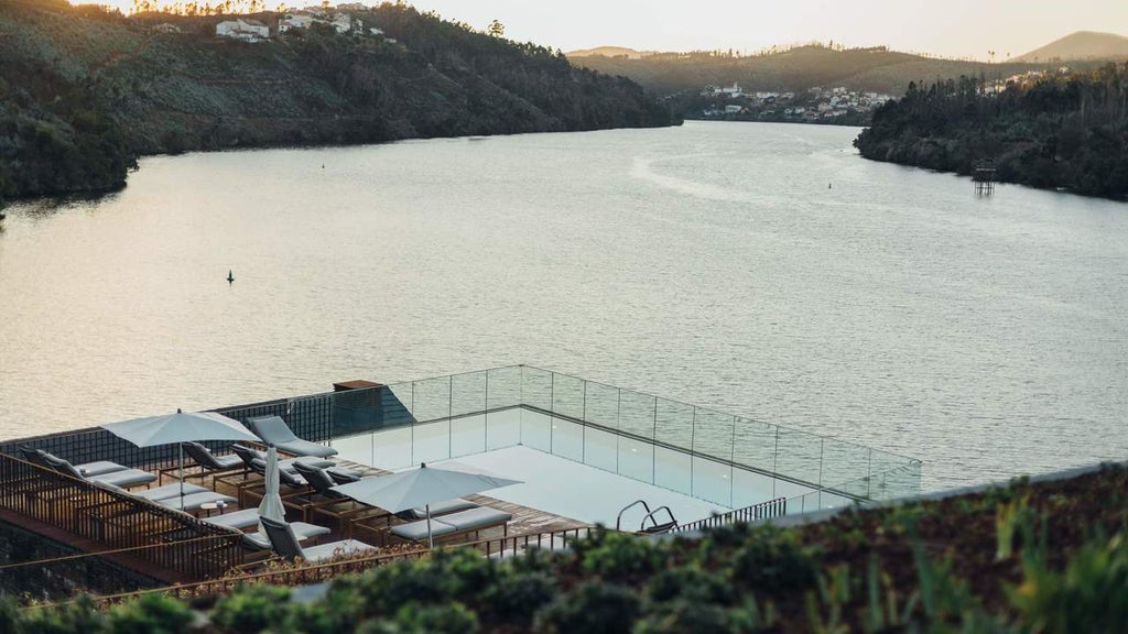 Luxury hillside hotel overlooking Douro River valley, featuring infinity pool, stone architecture and terraced vineyards at sunset