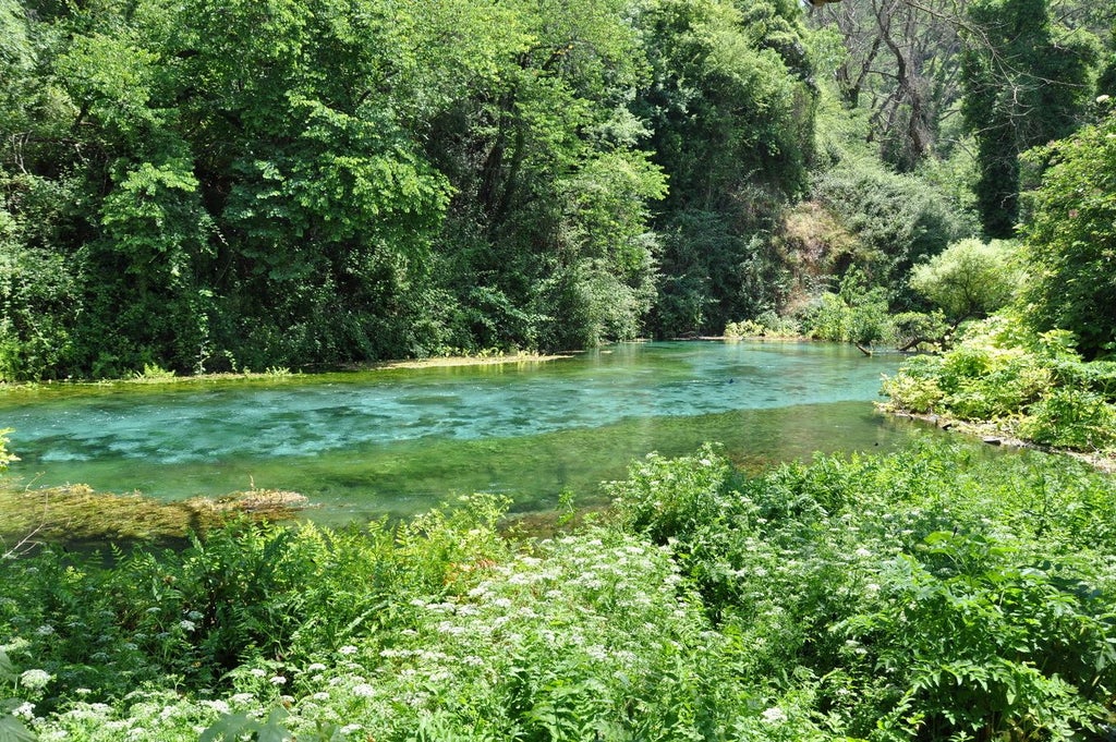 Turquoise waters of Blue Eye Spring cascading through lush Albanian landscape, with elegant dining setup featuring local gourmet cuisine against pristine natural backdrop