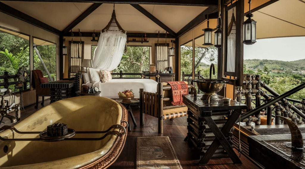 Luxurious safari-style tent suite with canopy bed, hardwood floors, private terrace overlooking lush Thai jungle and river views