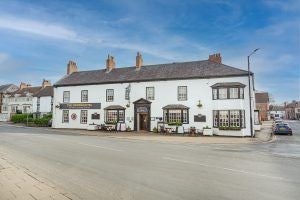 Elegant Georgian-style hotel exterior with stone facade, sash windows, and manicured gardens in historic Malton, North Yorkshire, United Kingdom