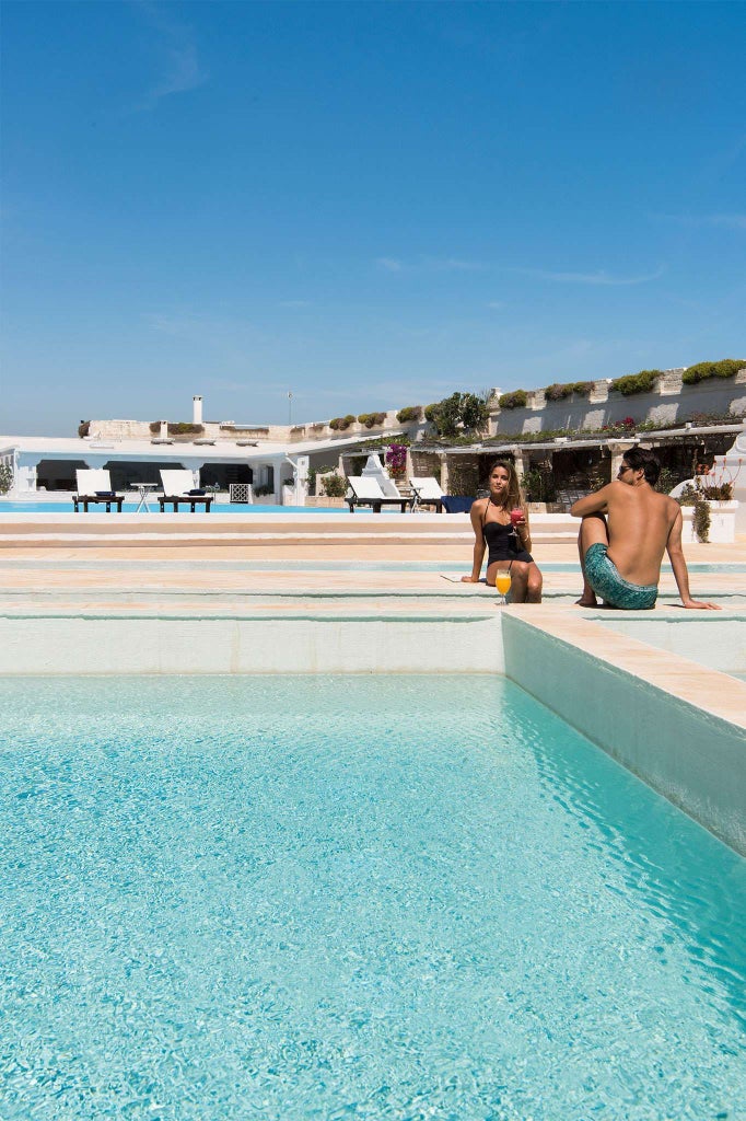 Luxurious seaside hotel with elegant infinity pool overlooking turquoise Mediterranean waters, surrounded by lush Italian coastal landscape near scenic shoreline