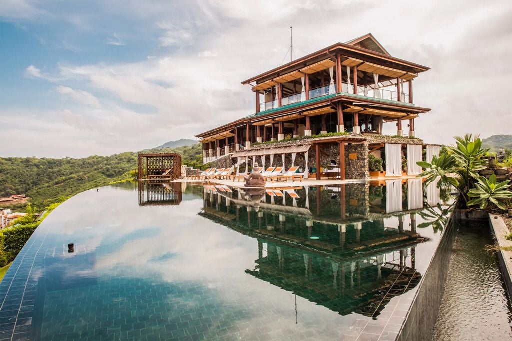 Infinity pool overlooking lush Costa Rican jungle and ocean at sunset, with wooden deck lounge chairs and tropical foliage