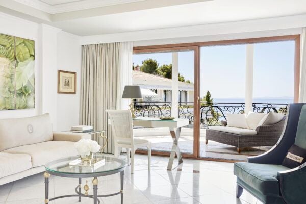 Spacious two-bedroom luxury suite with panoramic Aegean Sea views, elegant white furnishings, and private balcony at premier Greek coastal resort