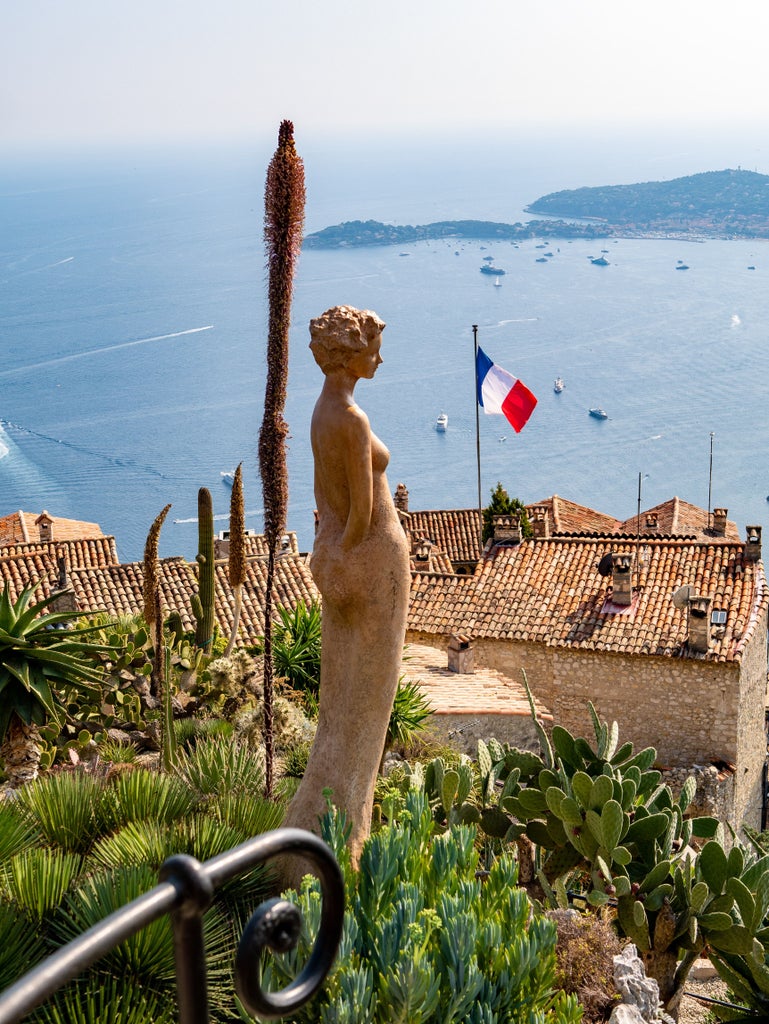 Panoramic view of the French Riviera coastline with luxury yachts in turquoise Mediterranean waters, framed by elegant palm trees and villas