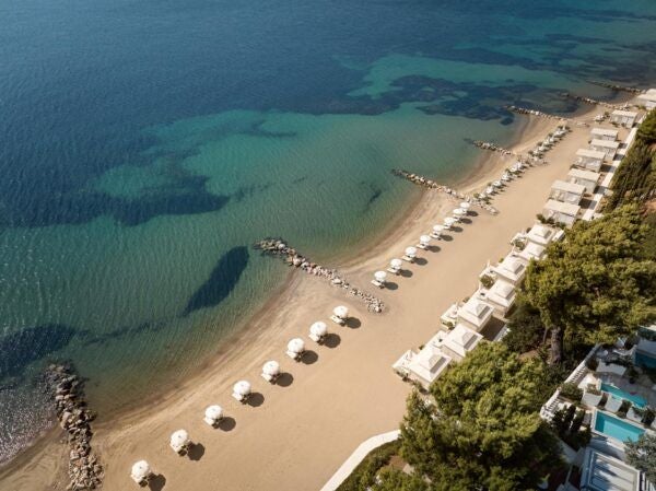 Luxurious beachfront resort with white Mediterranean architecture, azure Aegean waters, and elegant infinity pool overlooking pristine coastline