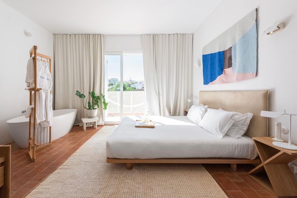 Bright, minimalist hotel room with whitewashed walls, rustic wooden beams, and a luxurious king bed draped in crisp white linens