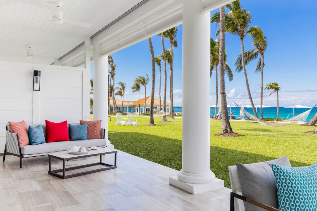 Luxurious oceanfront hotel with white colonial architecture, palm-lined infinity pool overlooking turquoise Caribbean waters at sunset