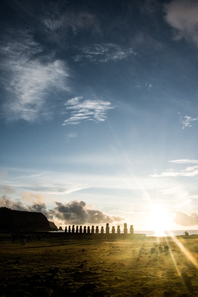 Towering ancient Moai stone statues stand sentinel against dramatic sunset sky on Easter Island's rugged coastal landscape