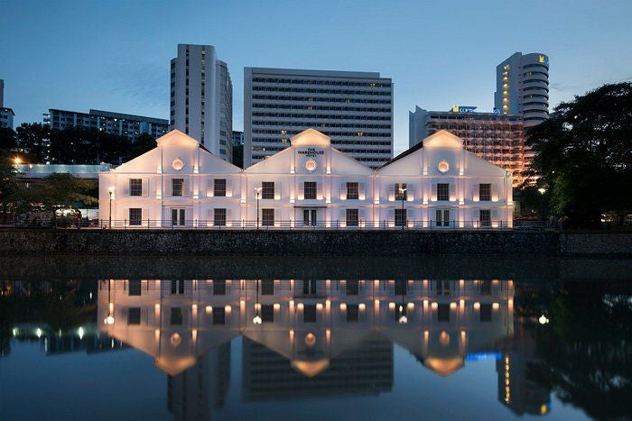 Historic warehouse turned luxury boutique hotel with industrial-chic facade, intricate metalwork and modern lighting along Singapore River