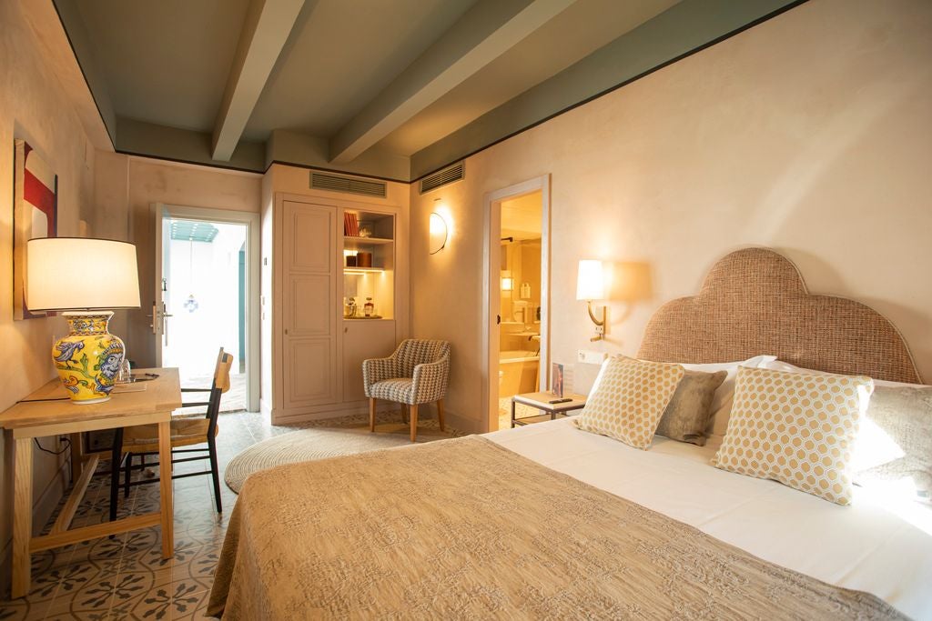 Elegant white-walled hotel room with traditional Spanish colonial architecture, plush bed, and soft natural light streaming through arched windows