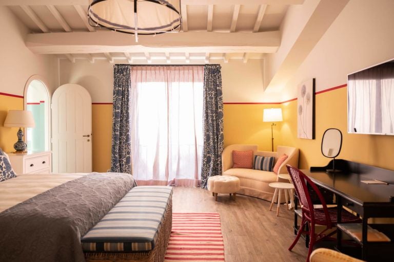 Elegant rustic Italian hotel room with soft cream walls, wooden beamed ceiling, and refined traditional furnishings in warm earthy tones