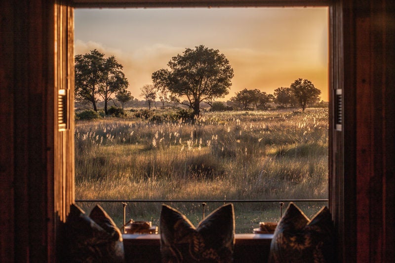 Elevated luxury safari tent overlooking flooded Okavango Delta plains, with wooden deck, canvas roof, and natural surroundings