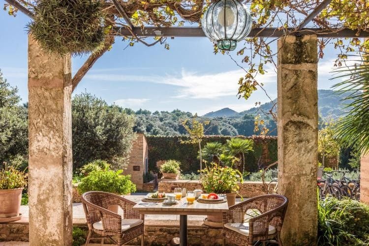 Spanish luxury rural hotel with stone facade, rustic wooden beams, and elegant outdoor dining area amid lush Mediterranean gardens