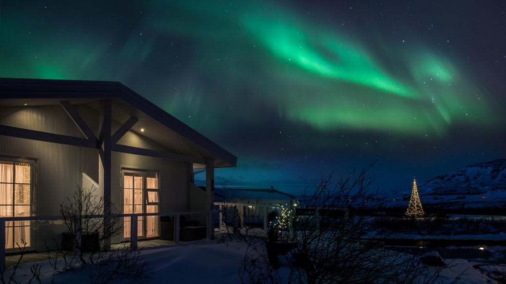 Modern luxury hotel with glass-walled rooms illuminated at night, set against snowy Icelandic landscape under starlit winter sky