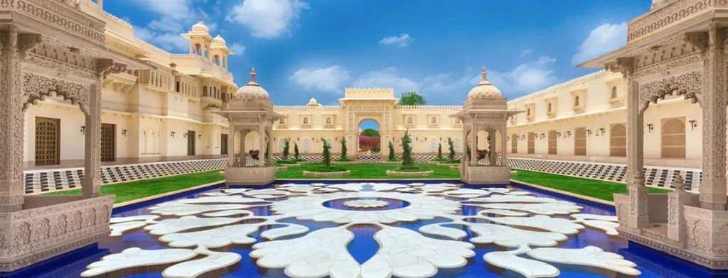 Elegant domed palace hotel in Udaipur with ornate Rajasthani architecture, white archways and reflection in serene infinity pools at sunset