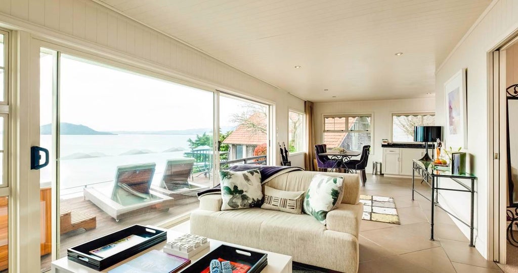 Luxurious lakeside cottage bedroom with expansive windows overlooking scenic New Zealand landscape, featuring modern decor and natural wooden accents