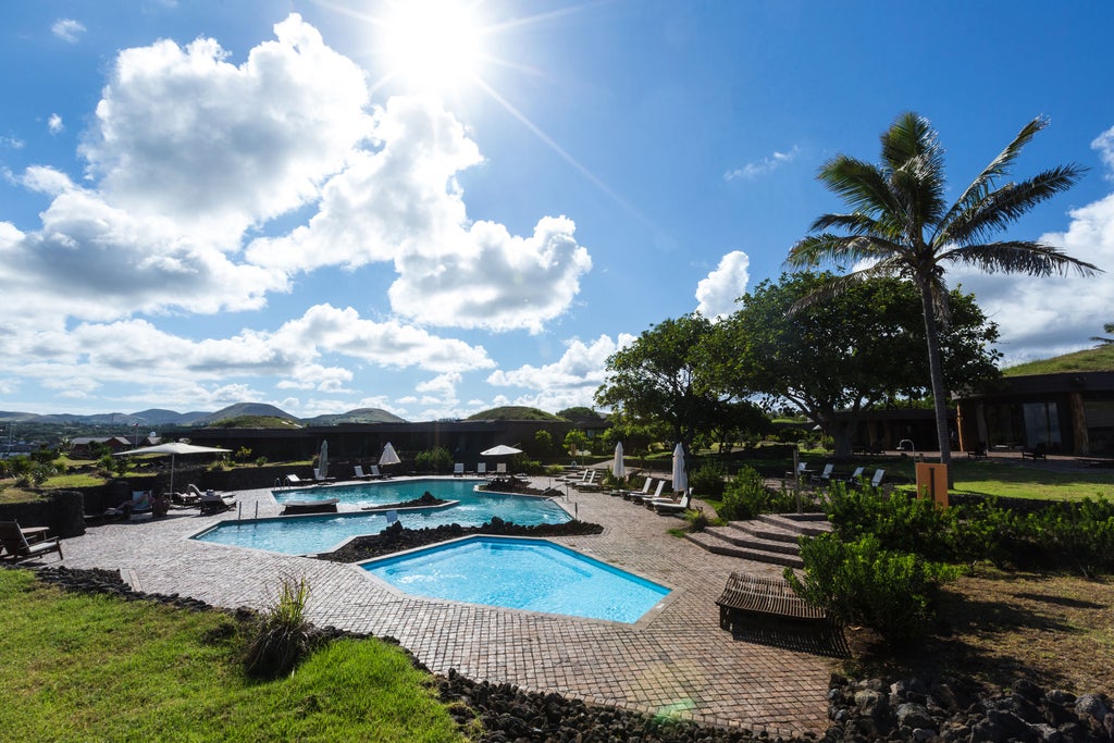 Modern beachfront hotel with curved architecture blending into rugged Easter Island terrain, featuring ocean-view suites and stone facades