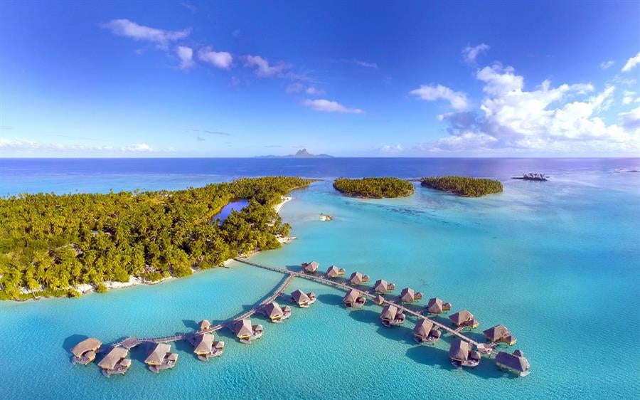 Luxurious overwater bungalows with thatched roofs connected by wooden walkways over crystal-clear turquoise lagoon in French Polynesia