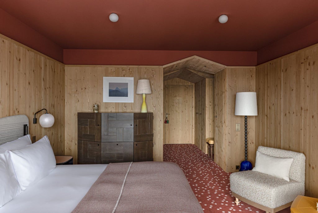 Luxurious alpine deluxe room with wooden accents, plush white bedding, expansive mountain view, and modern chalet-style design at Le Coucou Méribel hotel