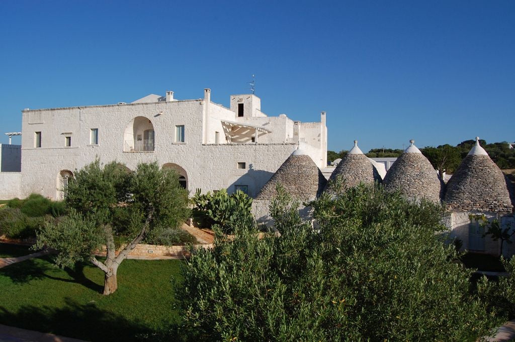 Rustic stone villa with elegant white-washed walls, surrounded by olive groves and rolling Puglia countryside at golden sunset