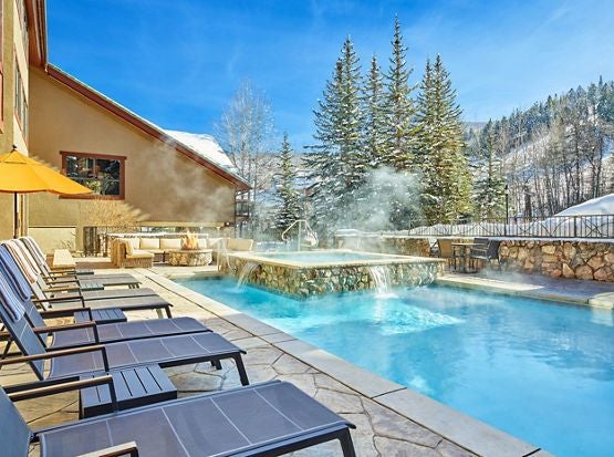 Luxurious mountain resort hotel nestled in scenic landscape, featuring stone facade, expansive windows, and elegant architectural design against dramatic natural backdrop