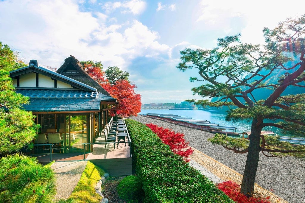 Traditional Japanese ryokan hotel with wooden exterior featuring a lantern-lit entrance path, surrounded by lush maple trees and stone gardens