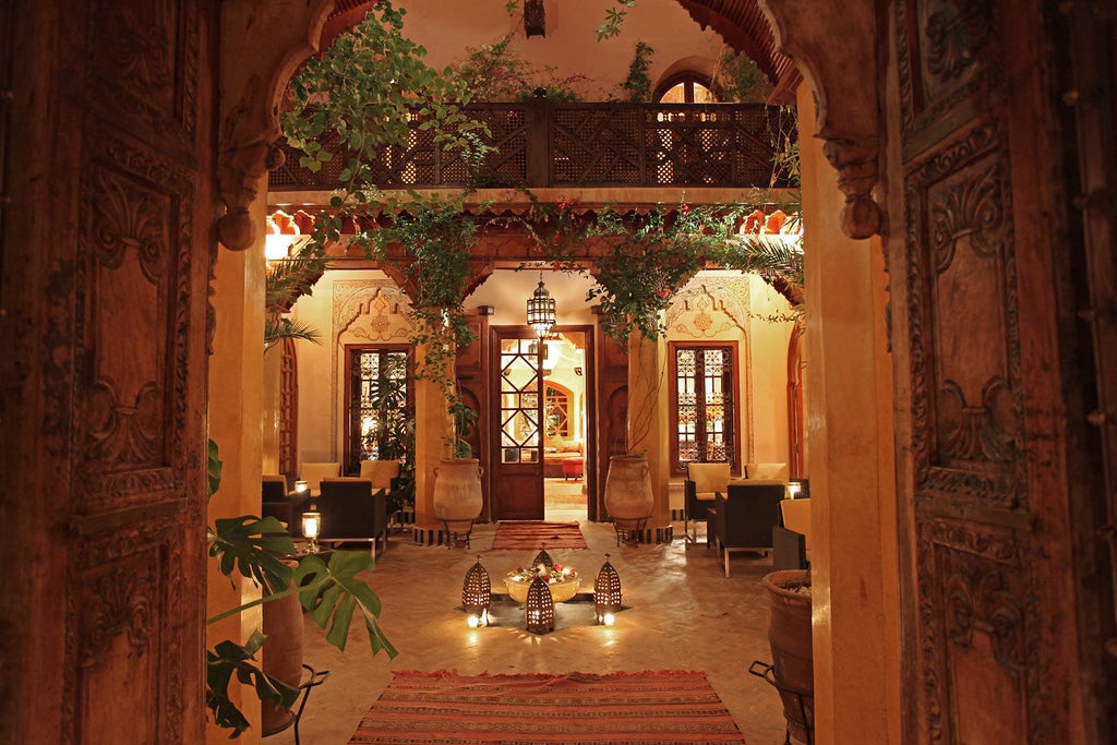 Elegant Moroccan hotel courtyard with ornate archways, traditional lanterns, and lush potted plants surrounding a tranquil reflecting pool