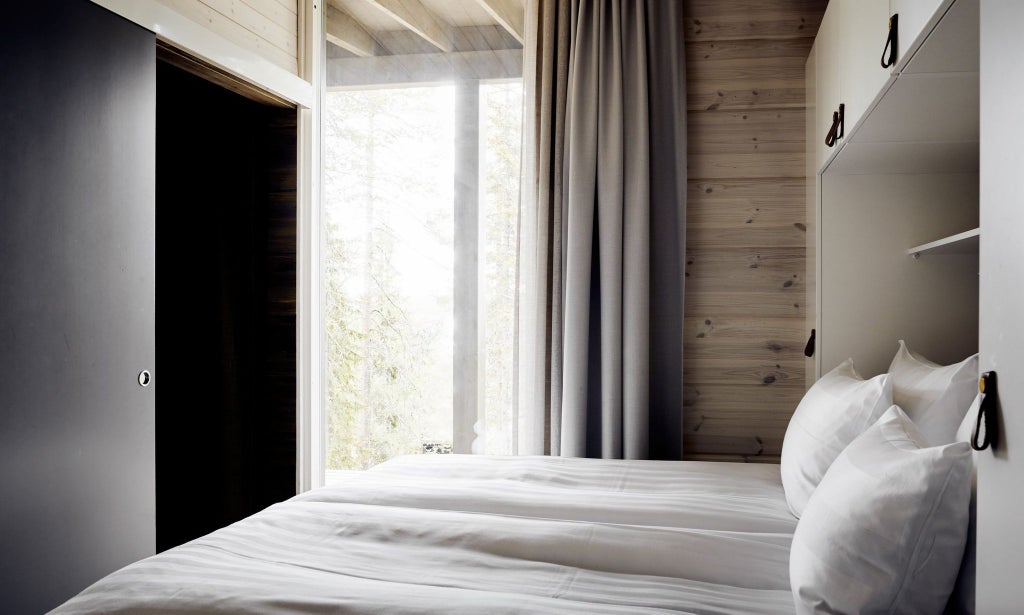 Modern Nordic hotel room with panoramic glass wall, cozy wooden interior, minimalist design, snow-covered pine forest view, plush white bedding, warm ambient lighting