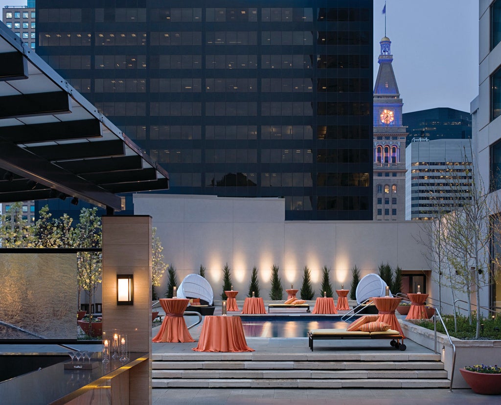 Modern glass skyscraper hotel with reflective blue windows, elegant stone facade, and upscale entrance with covered valet area in downtown Denver