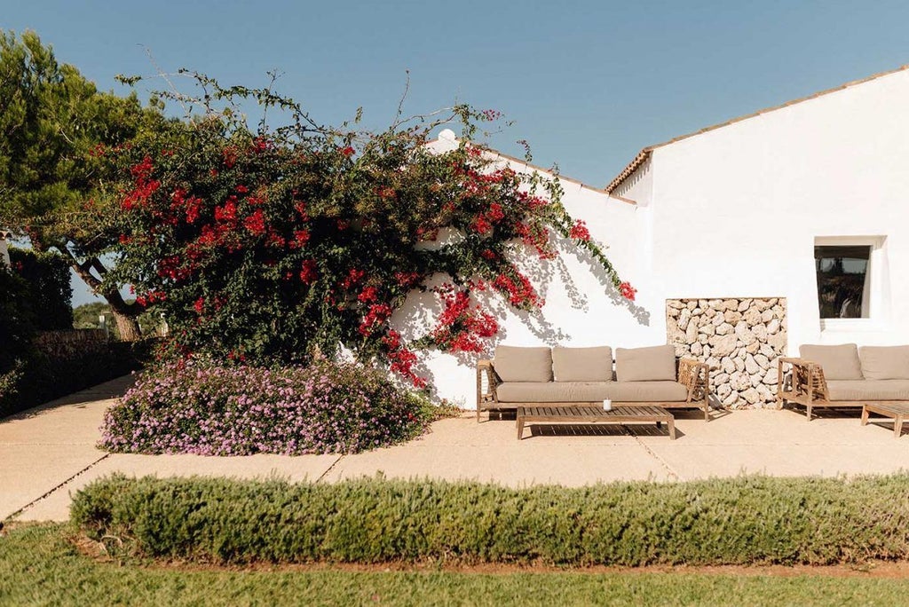 Whitewashed luxury boutique hotel nestled in Menorca's countryside, featuring stone walls, rustic terrace, and panoramic Mediterranean landscape view