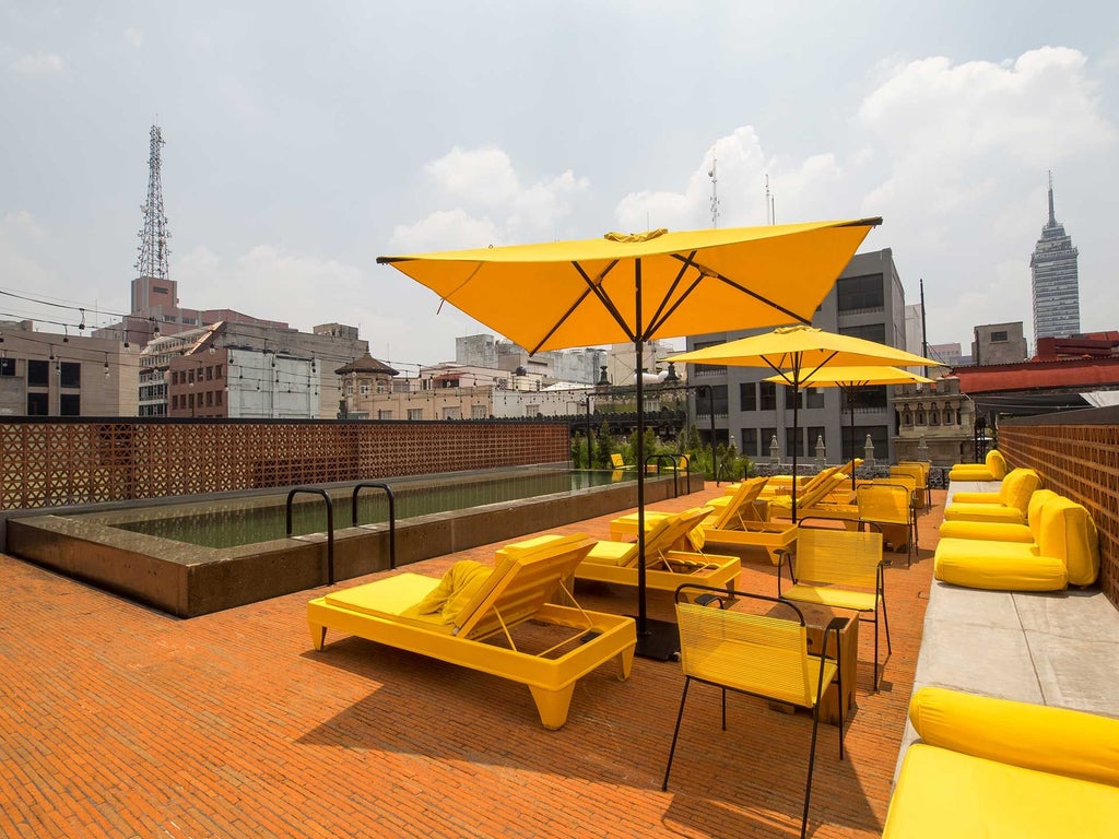 Elegant rooftop terrace of Downtown Mexico hotel, featuring colonial architecture, modern furnishings, and panoramic views of Mexico City's historic center at sunset