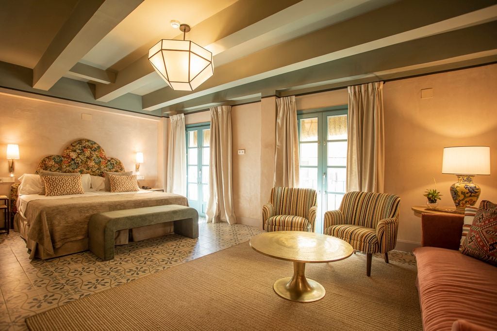 Elegant junior suite in Sevillian-style historic hotel, featuring white walls, wooden furnishings, and traditional Spanish architectural details with soft natural light