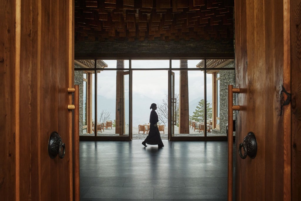 Contemporary lodge nestled in Bhutanese hillside with stone and timber facade, panoramic mountain views, and traditional architectural details