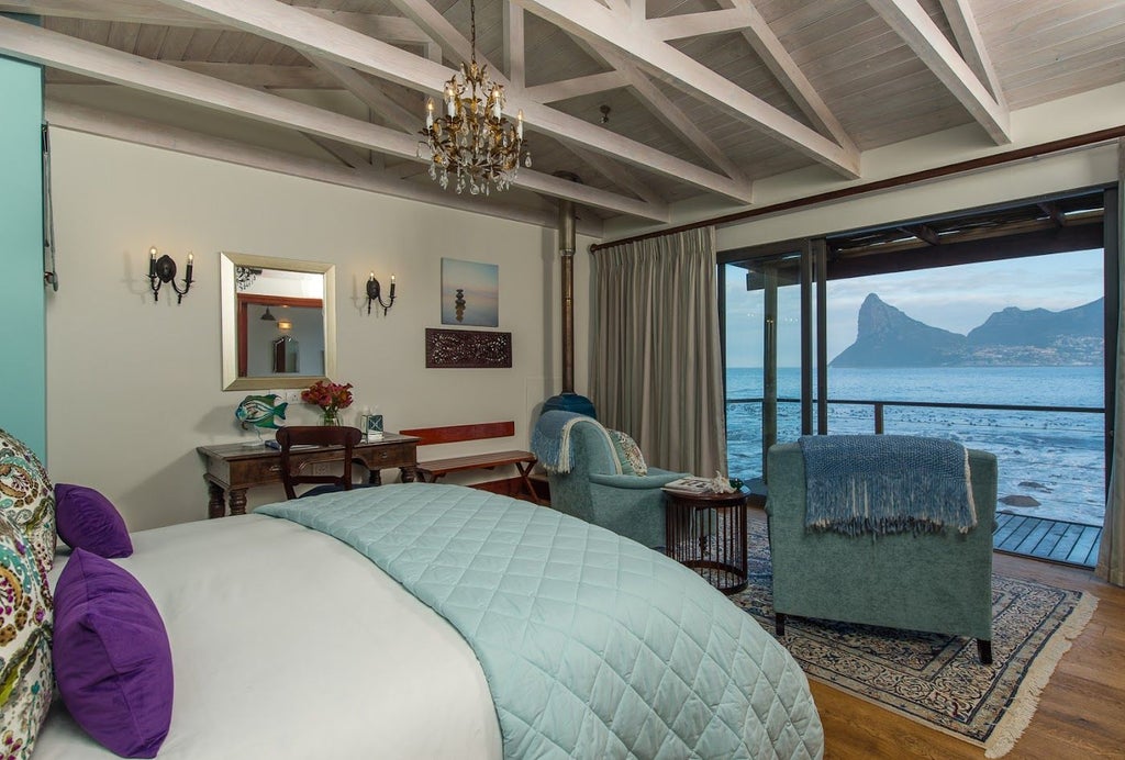 Luxury oceanfront lodge with infinity pool overlooking Chapman's Peak mountain and Atlantic waves crashing against rocky coastline at sunset