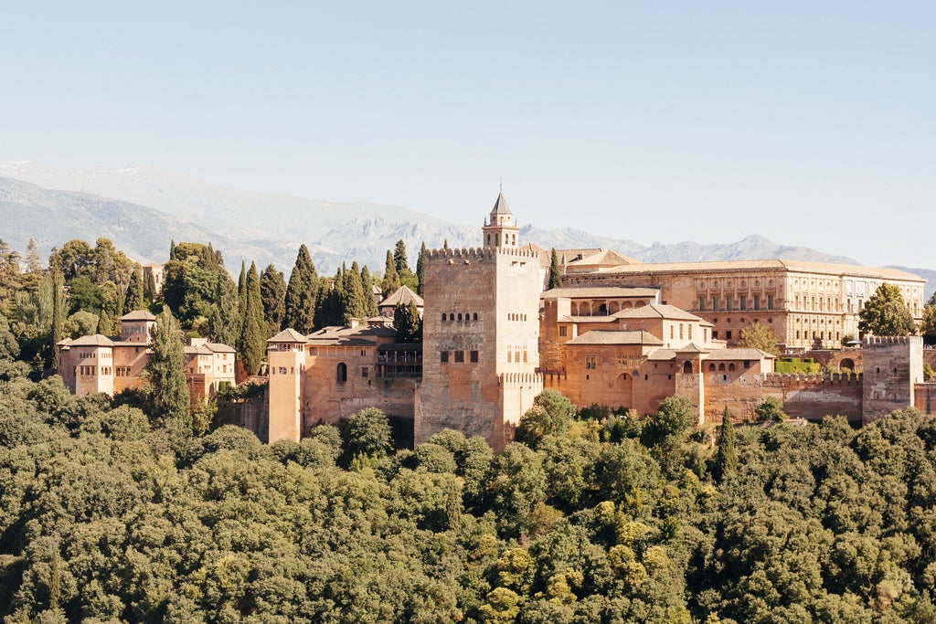 Ancient Moorish fortress of Alhambra overlooking Granada at twilight, with Sierra Nevada mountains and glowing city lights below