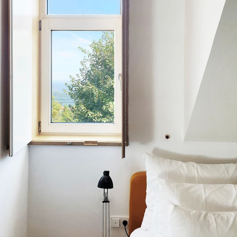 Elegant mountain-view junior suite with minimalist design, natural wood accents, white linens, and panoramic windows overlooking Portuguese landscape at Casa das Penhas Douradas