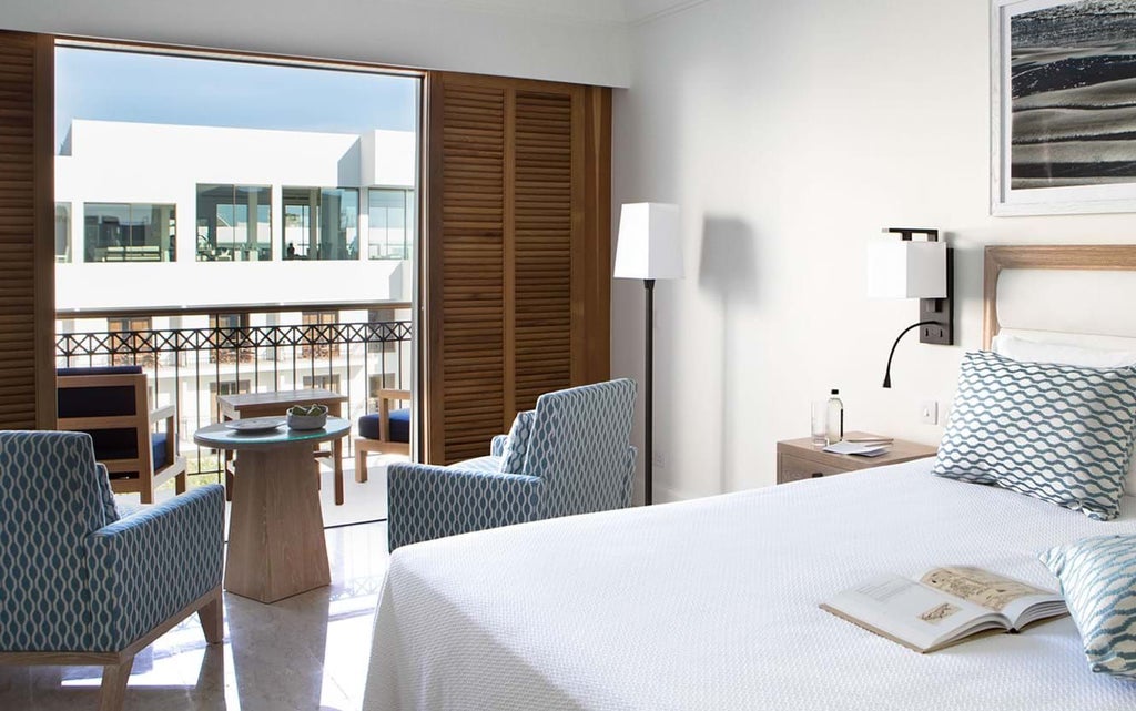 Elegant side sea view room with modern decor, white linens, panoramic windows overlooking azure Mediterranean waters at luxurious Cyprus coastal hotel