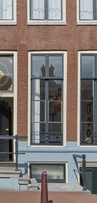 Elegant canal-side Pulitzer Amsterdam hotel with historic brick facade, arched windows, and ivy-covered walls reflecting in calm waters.