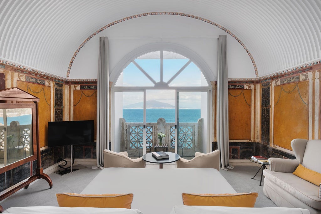 Elegant marble-clad suite with panoramic coastline view, ornate crystal chandelier, plush king bed, and refined Mediterranean decor in Sorrento luxury hotel