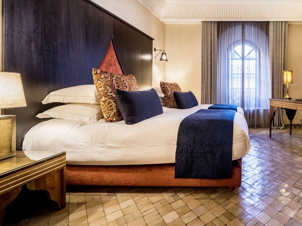 Elegant Moroccan deluxe hotel room with intricate tile work, luxurious four-poster bed, and traditional arabesque architectural details in soft neutral tones