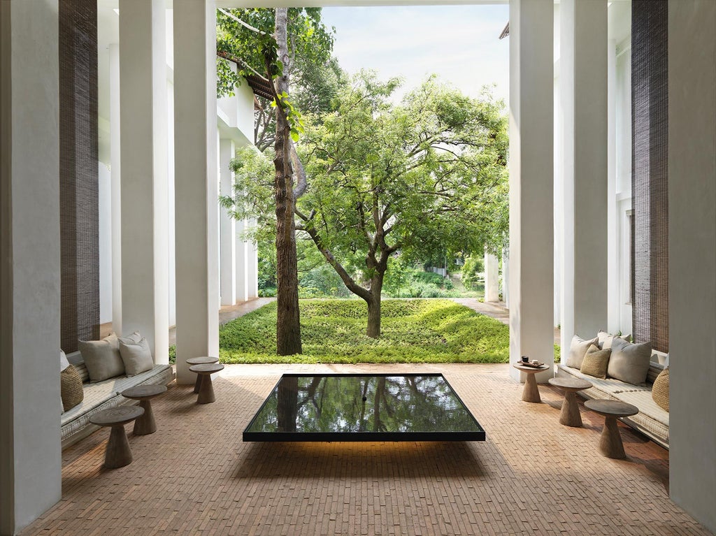 Contemporary Thai luxury hotel exterior with white stone walls, teak wood details, and lush tropical gardens framing open-air pavilions